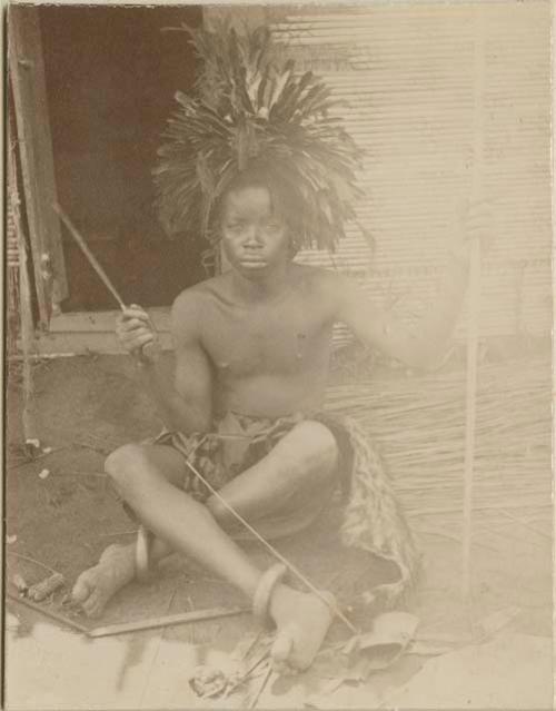 Man with headdress sitting in front of a structure