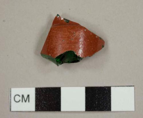 Emerald green bottle glass fragment with reddish-brown paint on the exterior