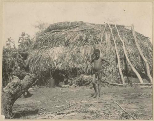 Man, woman and boy standing in front of a hut