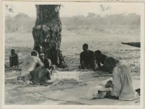 Group working on skins, man in foreground sewing kaross