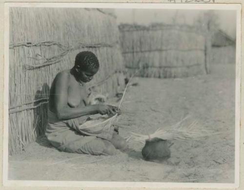 Woman sitting next to a hut making a basket