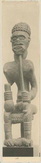 Wooden statue of a person seated and holding a club and resting his chin on a sceptre