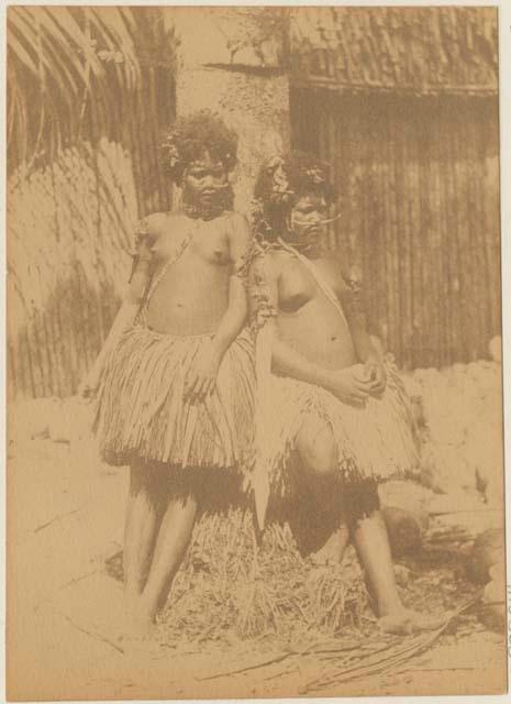 Two women leaning against a tree or post