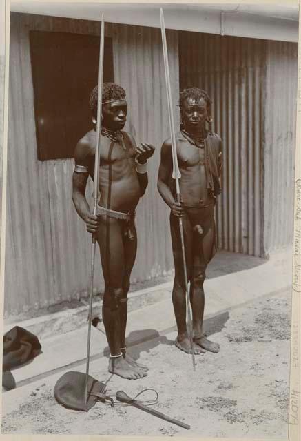 Two men with spears in front of a structure