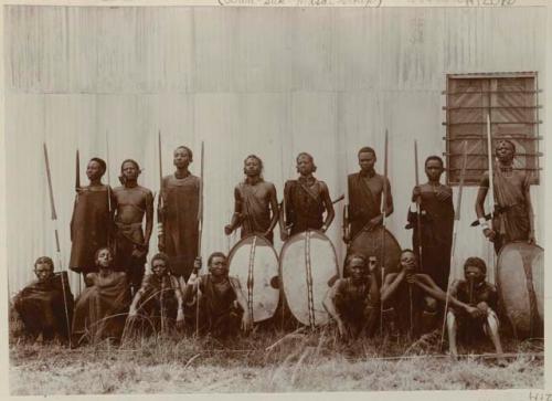 Group of men with spears and shields standing in front of a building