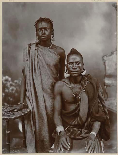 Studio portrait of two men, one sitting and one standing