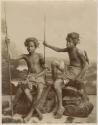 Studio portrait of two boys sitting and holding spears