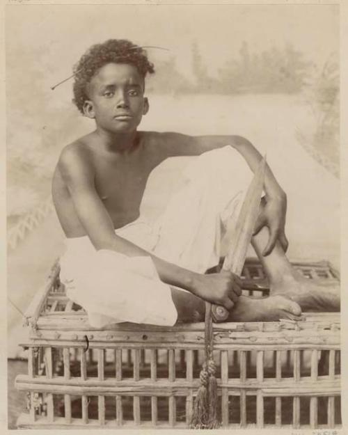 Studio portrait of a boy sitting on a trap holding a knife