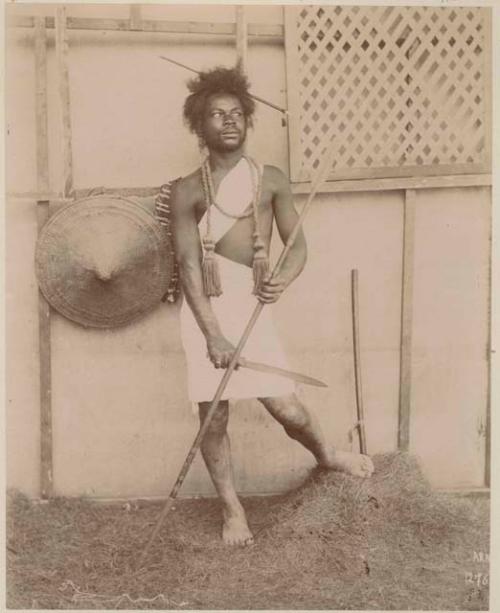 Man standing in front of a building holding a spear and knife