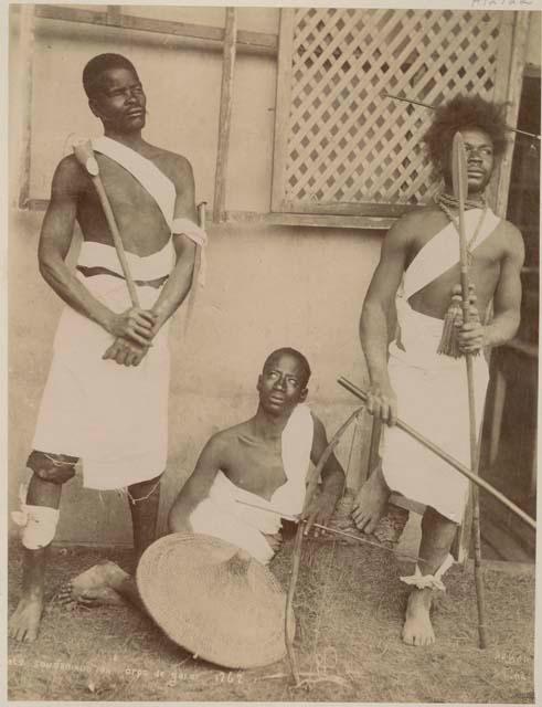 Three men with weapons in front of a building