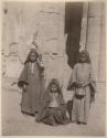 Three women with ceramic jars in front of an ancient building