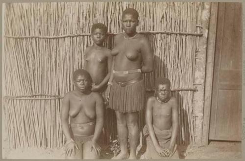 Two women and two children in front of a hut