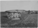 Woman sitting in front of menhir, with house in background