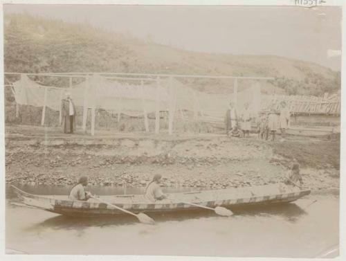 Three people in boat and group beside nets on shore