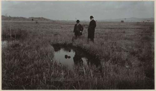 Two men standing next to excavation filled with water