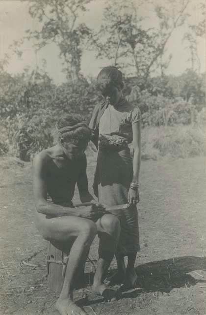 Tagbanua man writing by scratching onto bamboo, his wife watching him