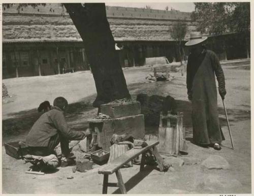 Man working tin in Market Square, with another man watching him