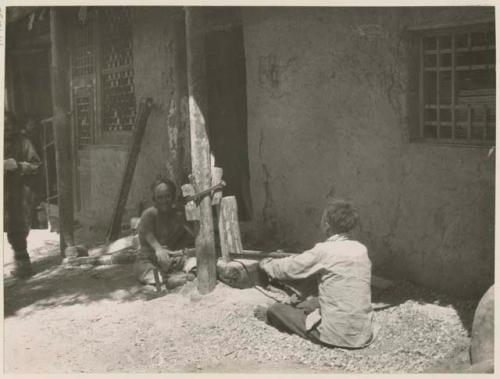 Two boys sawing wood in front of carpenter's shop