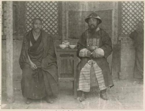 Man in his regalia with one of the head lamas sitting at a small table looking at the camera