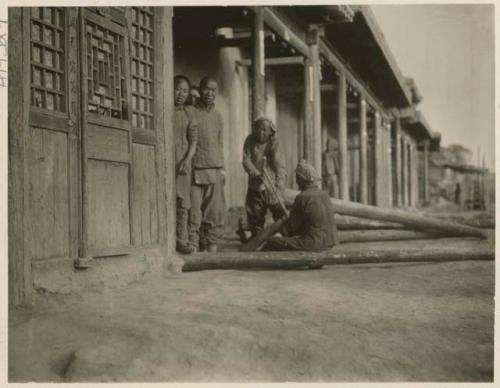 Boys sawing logs in front of carpenter shop