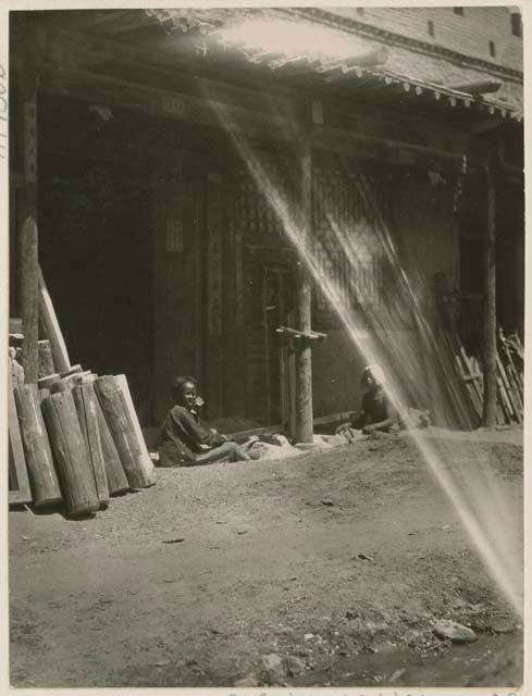 Boys sitting outside carpenter shop sawing wood