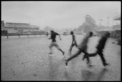 B/W image: Men running in a downpour, Mount Hagen bus terminal