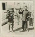 Two young boys carrying wooden buckets, one with a carrying pole