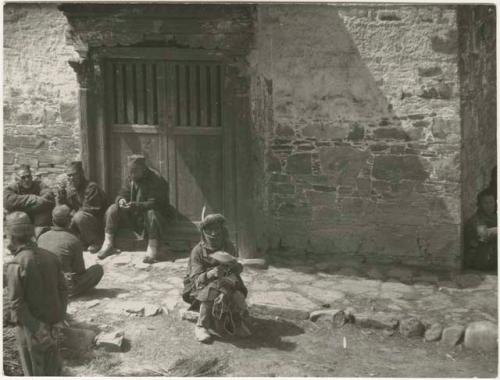 Man sitting outside building turning prayer wheel