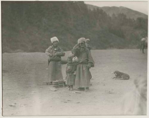 Women and children selling butter outside, with dog in background