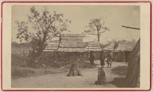 Men surrounded by buildings with thatched roofs