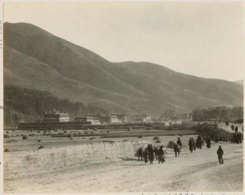 Pilgrims on the road to the lamasery of Labrang, Tibet, with the temple buildings and hills in the background