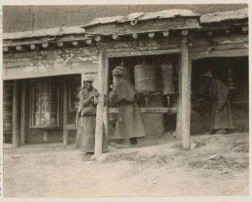 Two old women and one old man turning prayer wheels at a shed