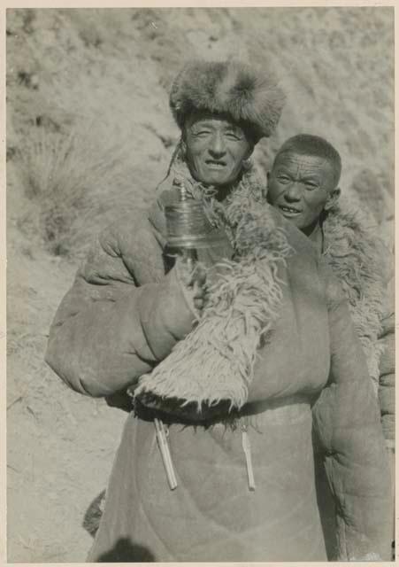 Two men standing outside, one holding prayer wheel