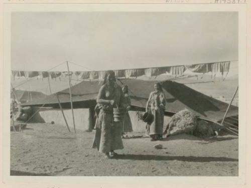 Three women standing outside of tent, holding buckets