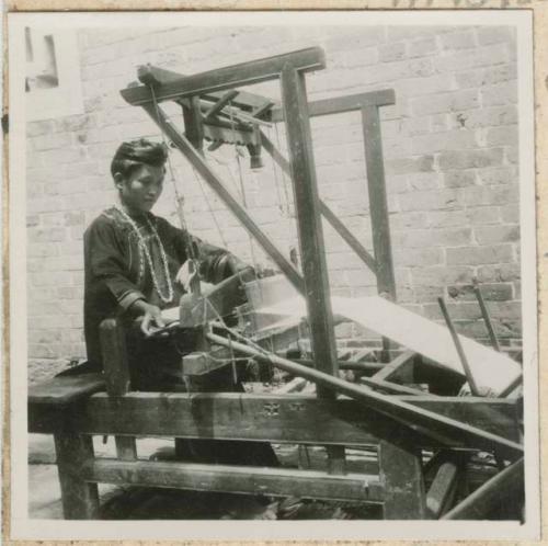 Woman weaving with a loom outside a building