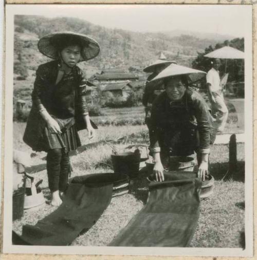 Women in conical hats washing and drying woven cloth outside