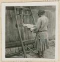 Woman weaving with a back strap loom outside a building