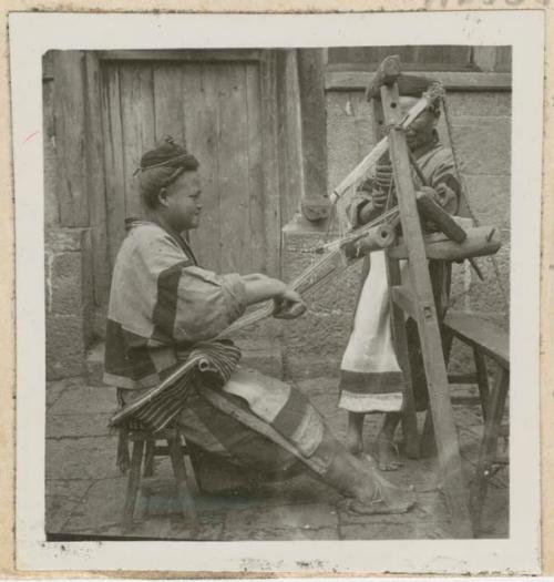 Woman weaving using back strap loom, with another woman in the background