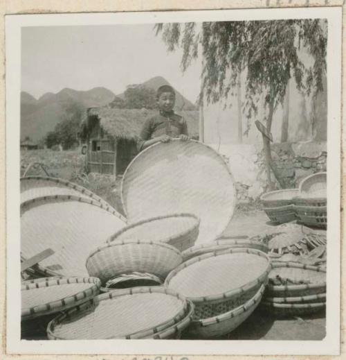 Piles of market baskets outside, one held by a boy