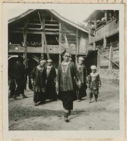 People in headresses and batik skirts next to a building