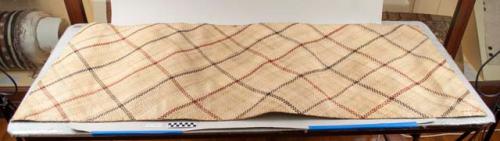 Sleeping mat of fine natural fibres. Design of red and black intersecting lines.