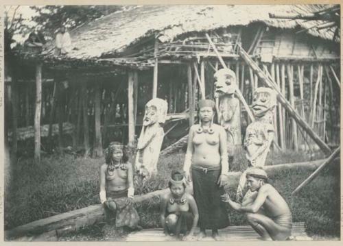 Man and three women standing in front of wooden figures and a structure