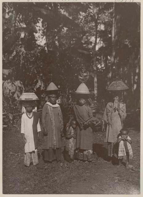 Four women and two children outside, the women in traditional hats
