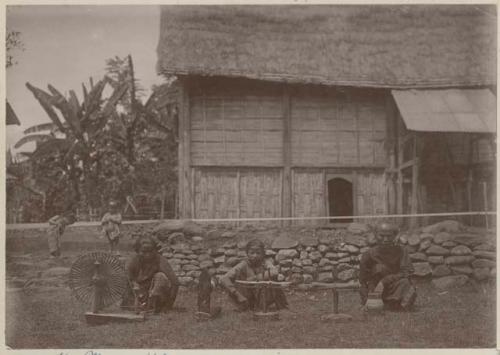 Three women sitting outside spinning with a wheel and other equipment