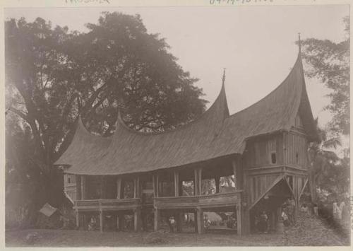 Thatched council building on stilts, with people around it