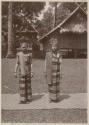 Two women standing outside on a mat in traditional dress