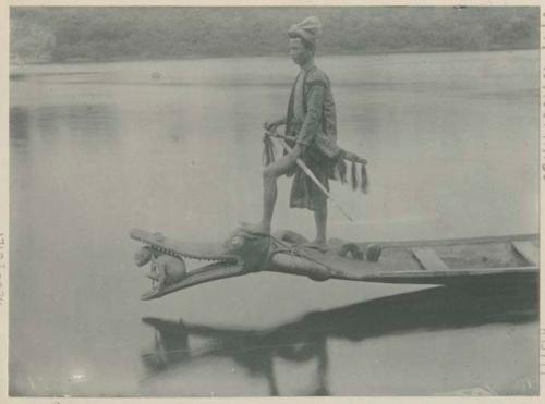 Man standing at bow of canoe, carved in shape of crocodile with animal in open mouth