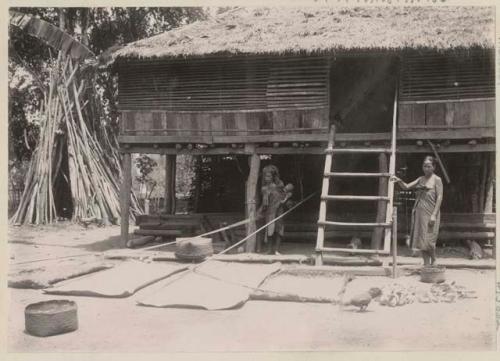 Two women, baby and a chicken in front of a building with mats laid out in front
