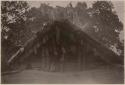 People in front of thatched structure with carved wooden posts