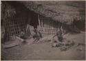 People weaving mats in front of a building